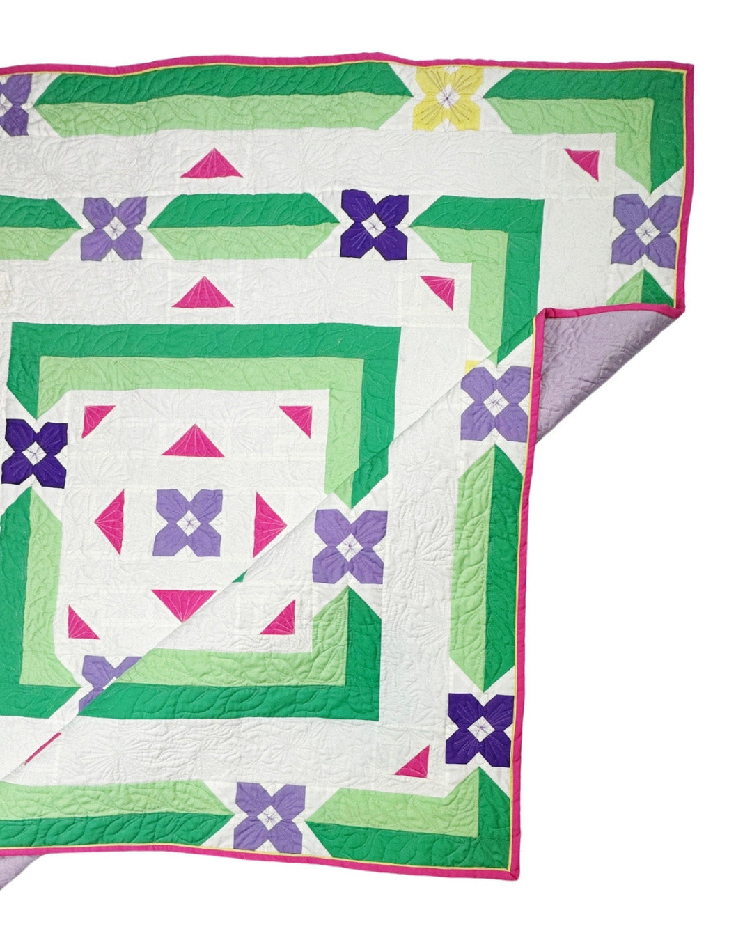 Albion Blooms quilt. A geometric quilt with small flower motifs surrounded by repeating medallion strips and triangles. Made in purple, pink, yellow, and green fabrics on a white background. Displayed flat on a white surface with the corner folded.