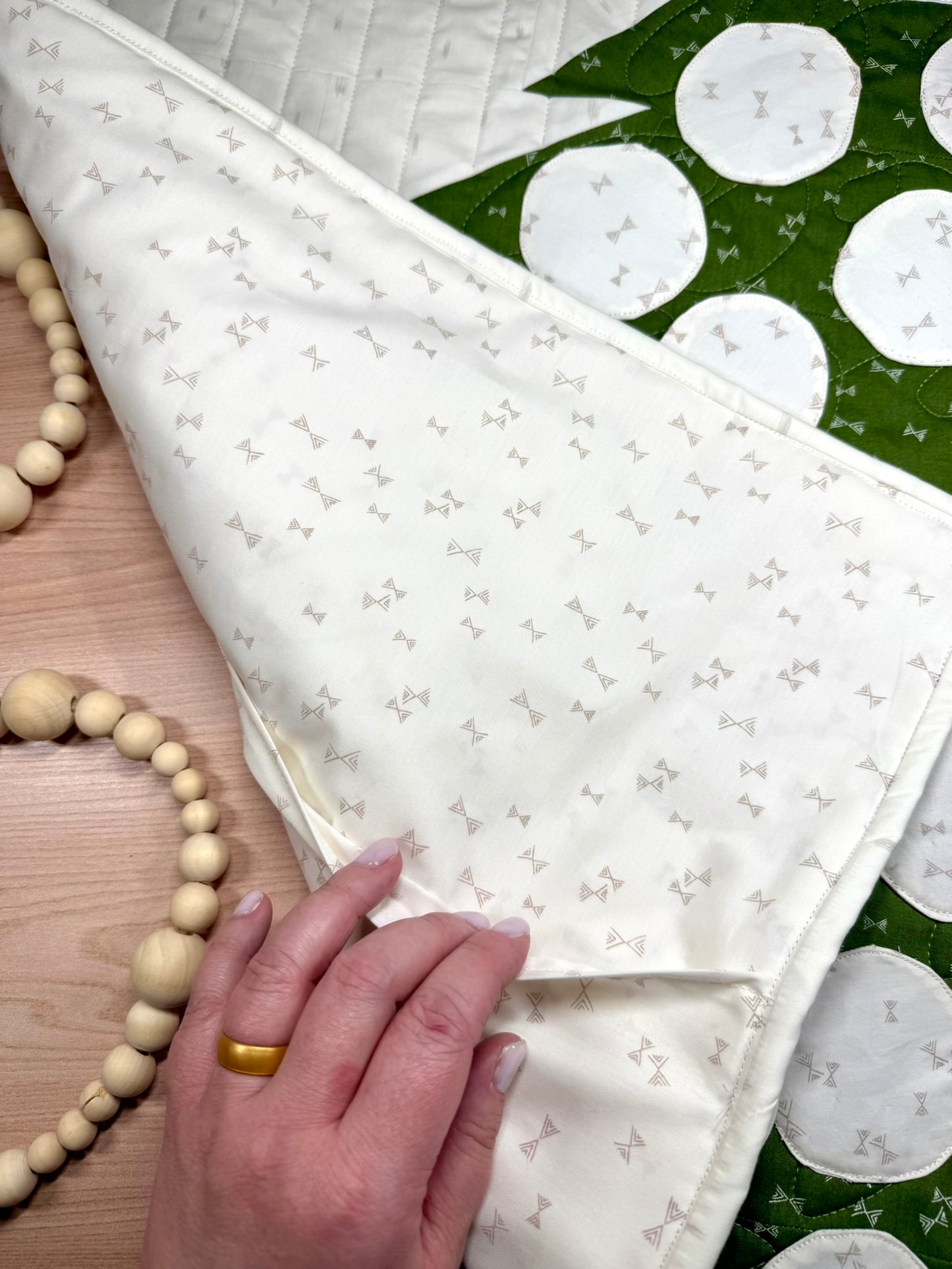 Merry Mini Advent quilt. A small quilt resembling the side of a green patchwork Christmas tree with white circle ornament pockets. Made as a pillow cover. Displayed flat with the corner folded to illustrate the pillow pocket opening.