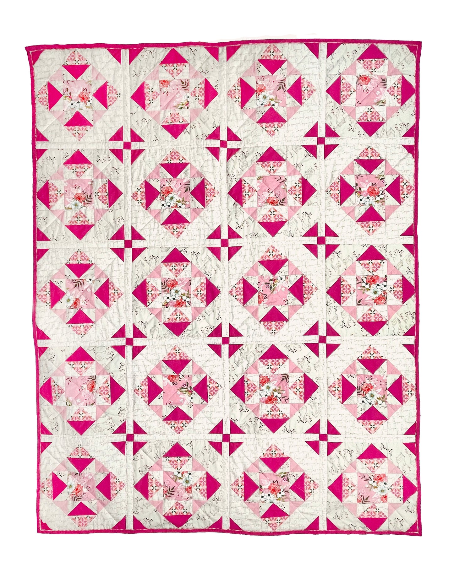 Alta Blooms quilt. A geometric quilt with a small star motif and triangular accents. Bright and medium pinks on a light cream background. Displayed flat on a white surface.