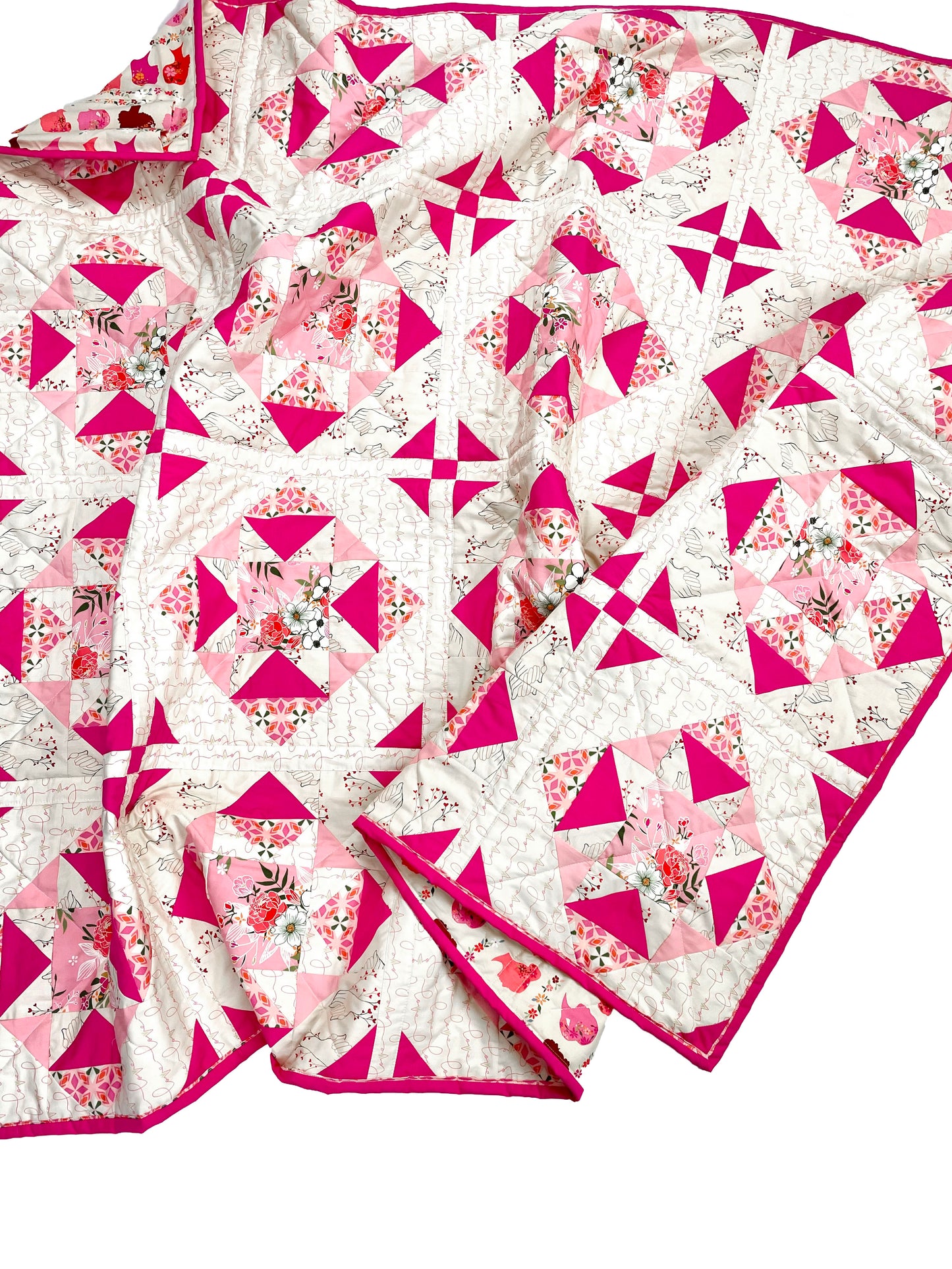 Alta Blooms quilt. A geometric quilt with a small star motif and triangular accents. Bright and medium pinks on a light cream background. Displayed on a white surface, slightly crumpled.