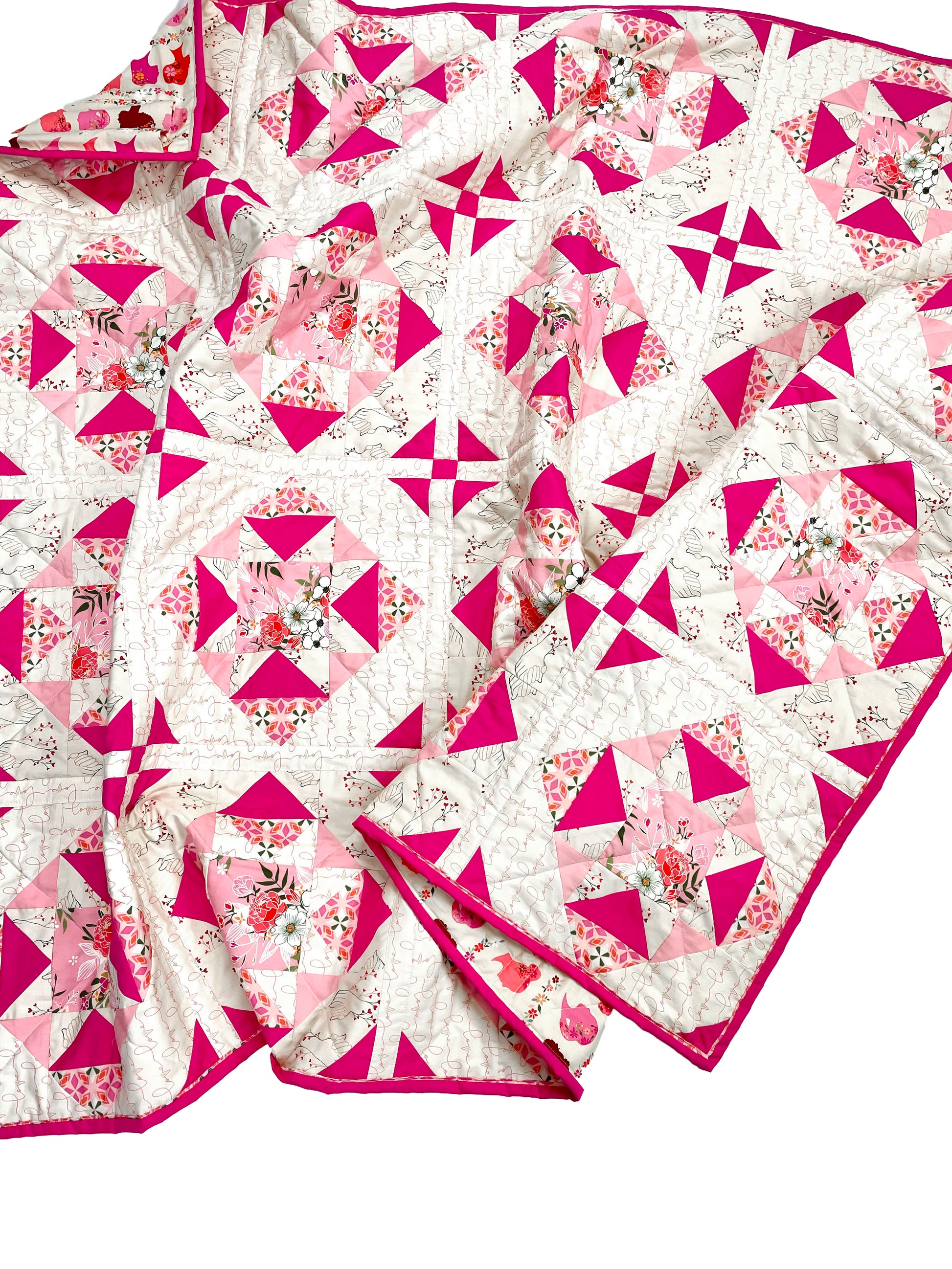 Alta Blooms quilt. A geometric quilt with a small star motif and triangular accents. Bright and medium pinks on a light cream background. Displayed on a white surface, slightly crumpled.