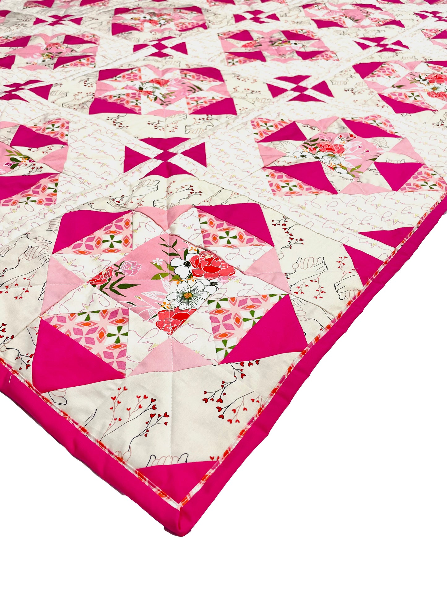 Alta Blooms quilt. A geometric quilt with a small star motif and triangular accents. Bright and medium pinks on a light cream background. Displayed flat on a white surface, focused on the corner.