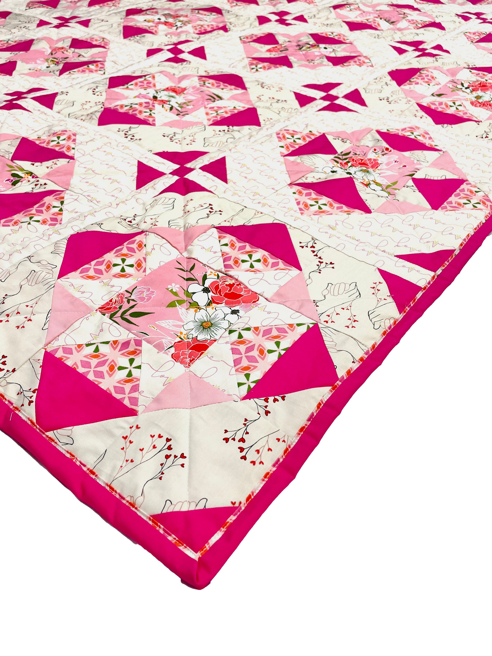 Alta Blooms quilt. A geometric quilt with a small star motif and triangular accents. Bright and medium pinks on a light cream background. Displayed flat on a white surface, focused on the corner.