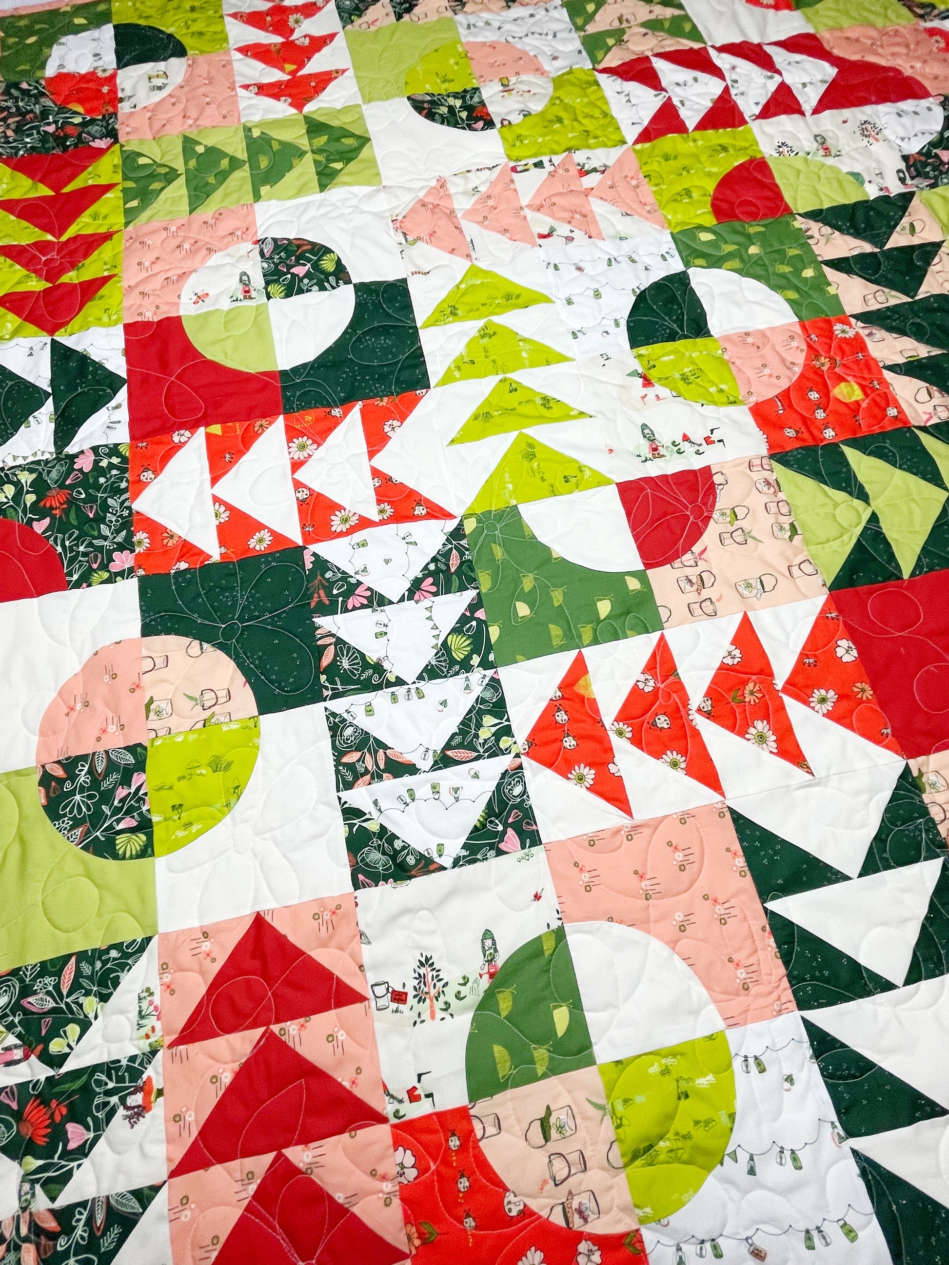 Carrol’s Garden quilt. A geometric quilt with quarter circles distributed with groups of four flying geese. Made of green, red, peach, and white fabrics. Displayed flat and viewed closely.