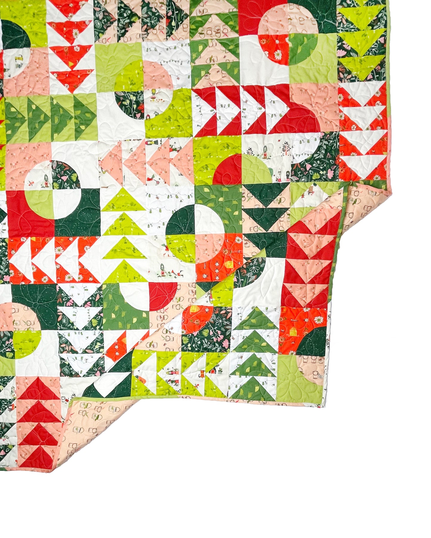 Carrol’s Garden quilt. A geometric quilt with quarter circles distributed with groups of four flying geese. Made of green, red, peach, and white fabrics. Displayed flat on a white surface with the corner folded.