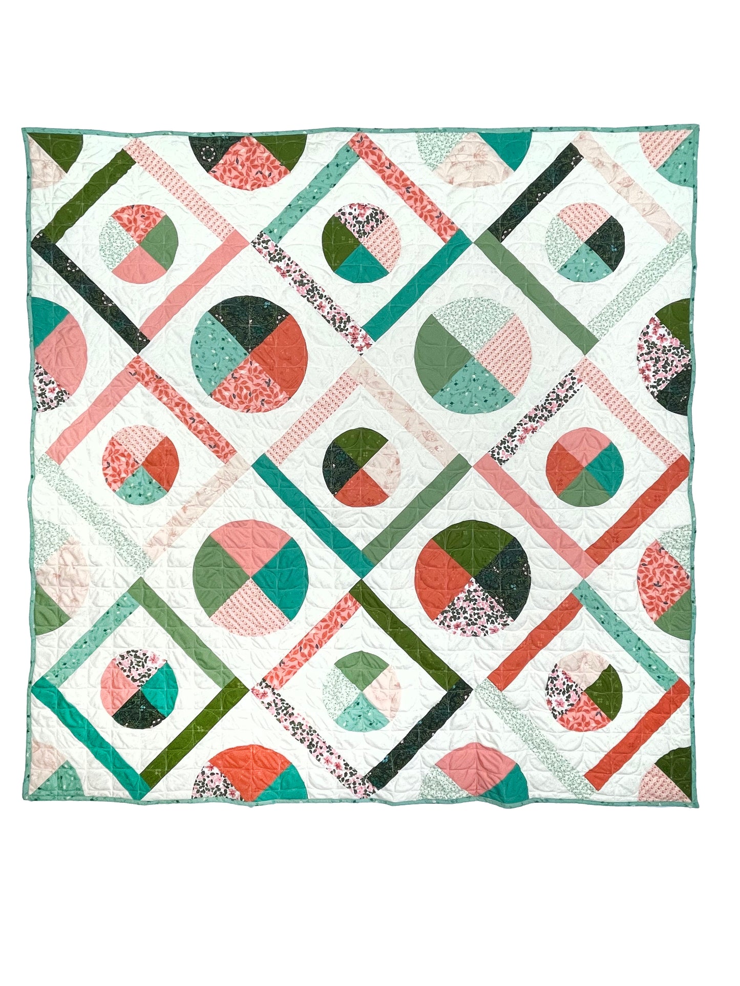 Dora May quilt. A geometric quilt with quarter circles and straight fabric strips in a diamond shape. Made of teal, olive, pink, and orange floral fabrics on a light background. Displayed flat on a white surface.