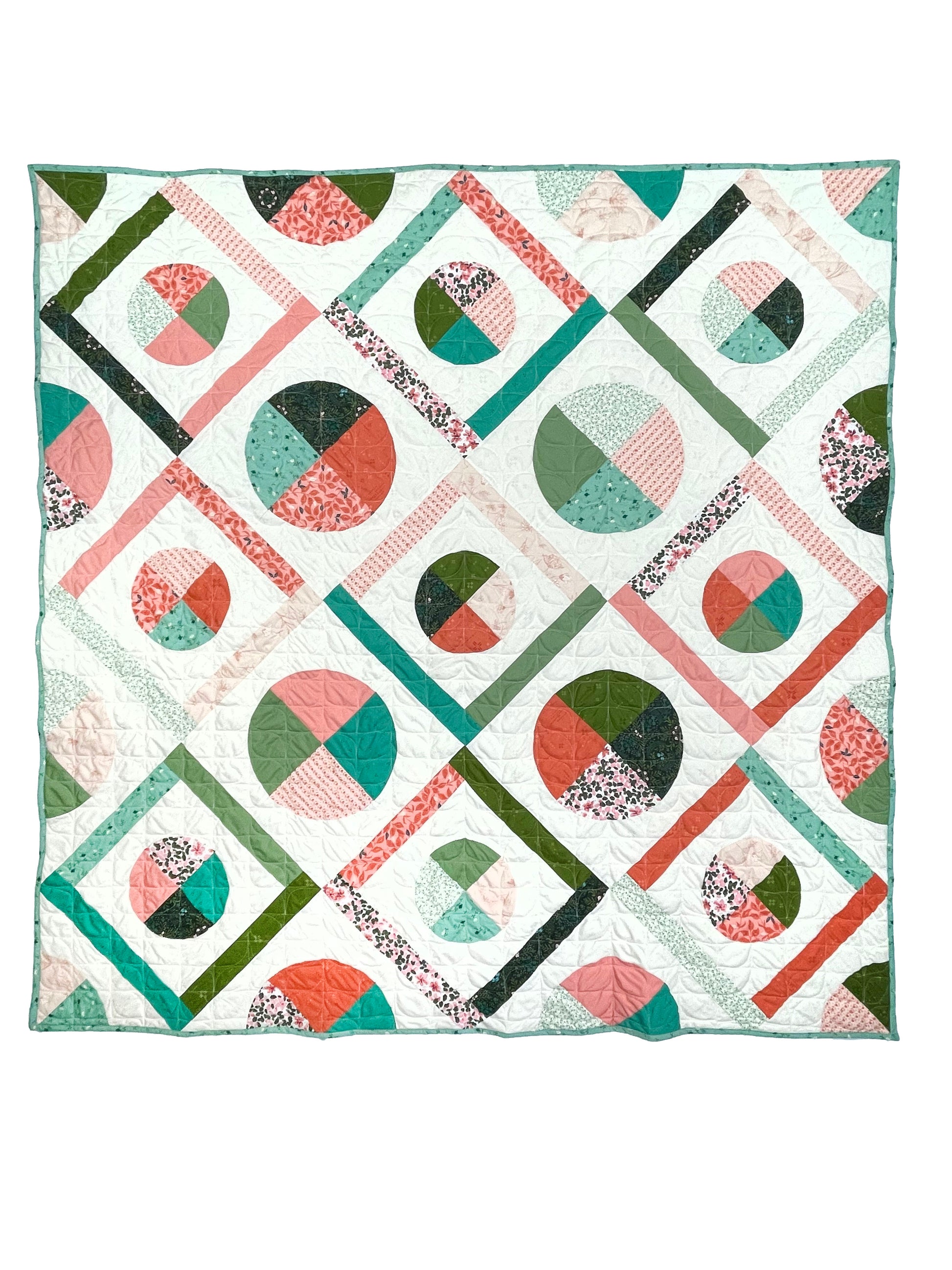 Dora May quilt. A geometric quilt with quarter circles and straight fabric strips in a diamond shape. Made of teal, olive, pink, and orange floral fabrics on a light background. Displayed flat on a white surface.
