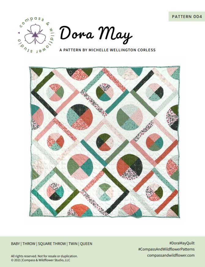 Dora May quilt pattern cover. A geometric quilt with quarter circles and straight fabric strips in a diamond shape. Made of teal, olive, pink, and orange floral fabrics on a light background. Name of quilt and company logo.