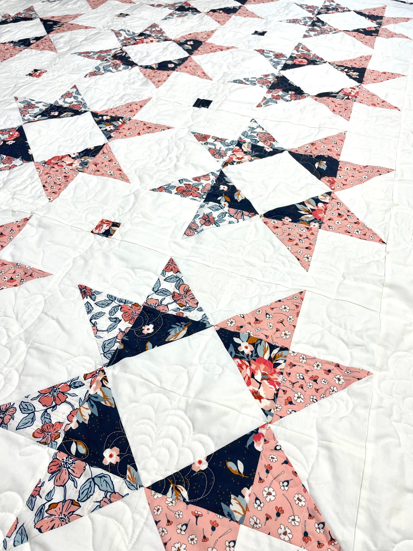 Lilian Star quilt. A geometric star quilt made with peach and navy fabrics on a white background, viewed close up on an angle.