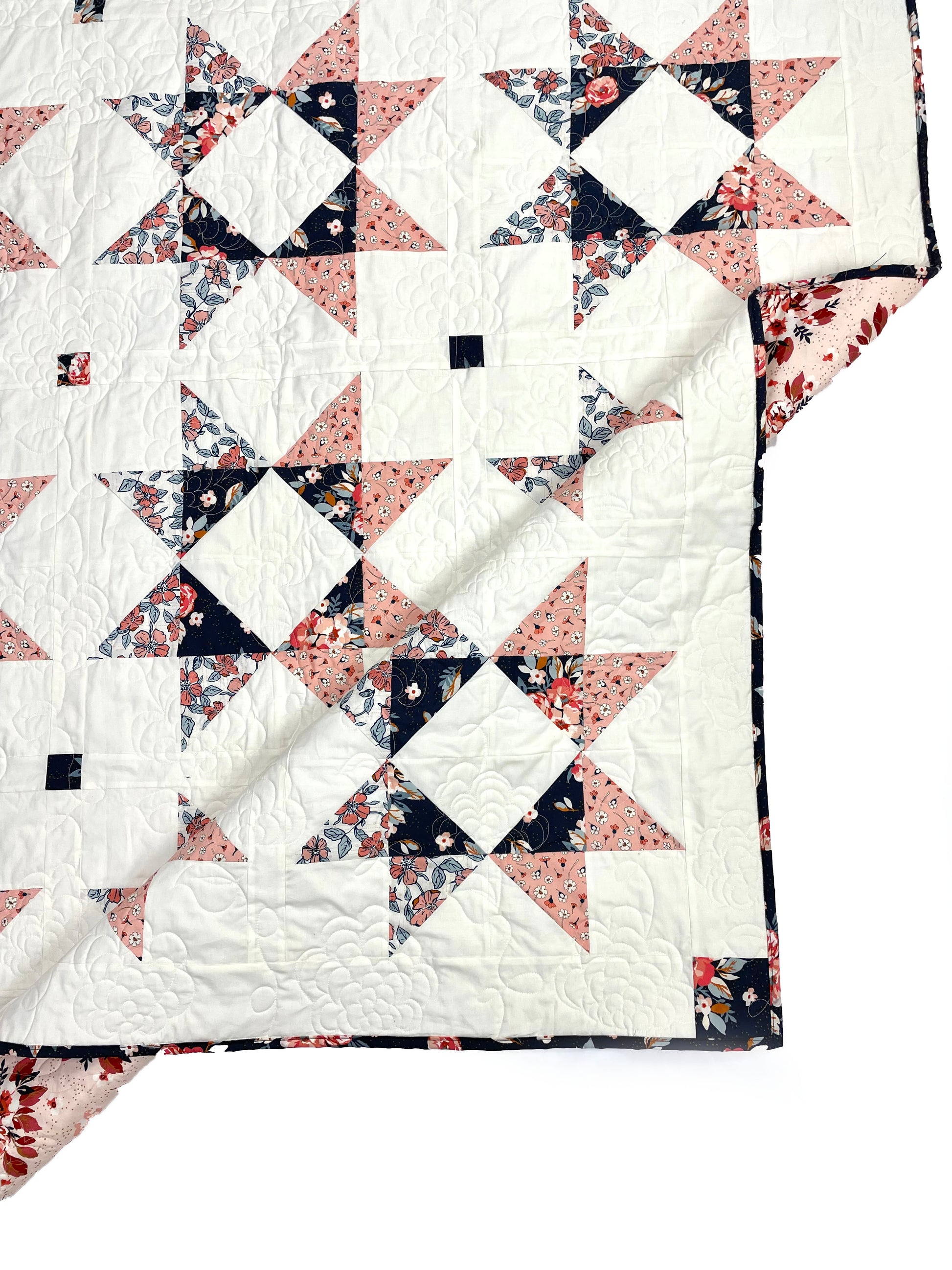 Lilian Star quilt. A peach and navy star quilt with a white background. Displayed semi-folded on a white floor.