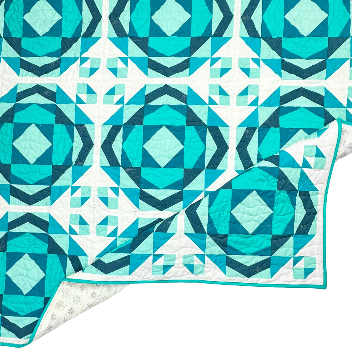 Millcreek quilt. A geometric quilt with a repeating motif that mimics water ripples. Made in varied shades of teal blue with a white background. Displayed flat on a white surface with the corner folded.