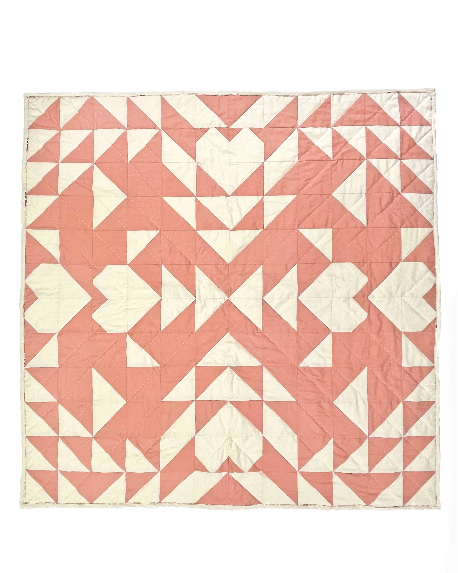 Sweet LaNora quilt. A geometric quilt with triangle and heart motifs made of fabric with ivory and peach tones.  Displayed flat on a white surface.