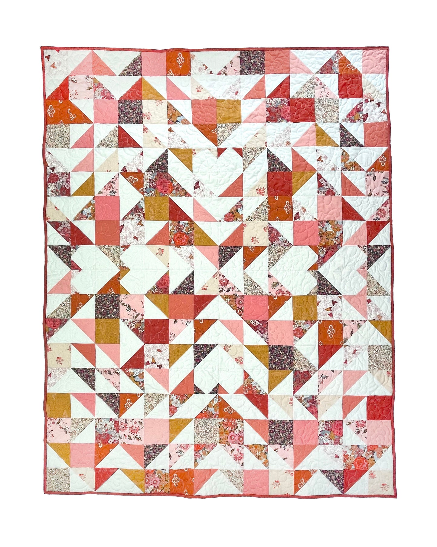 Sweet LaNora quilt. A geometric quilt with triangle and heart motifs made of fabric with red and peach tones.  Displayed flat on a white surface.