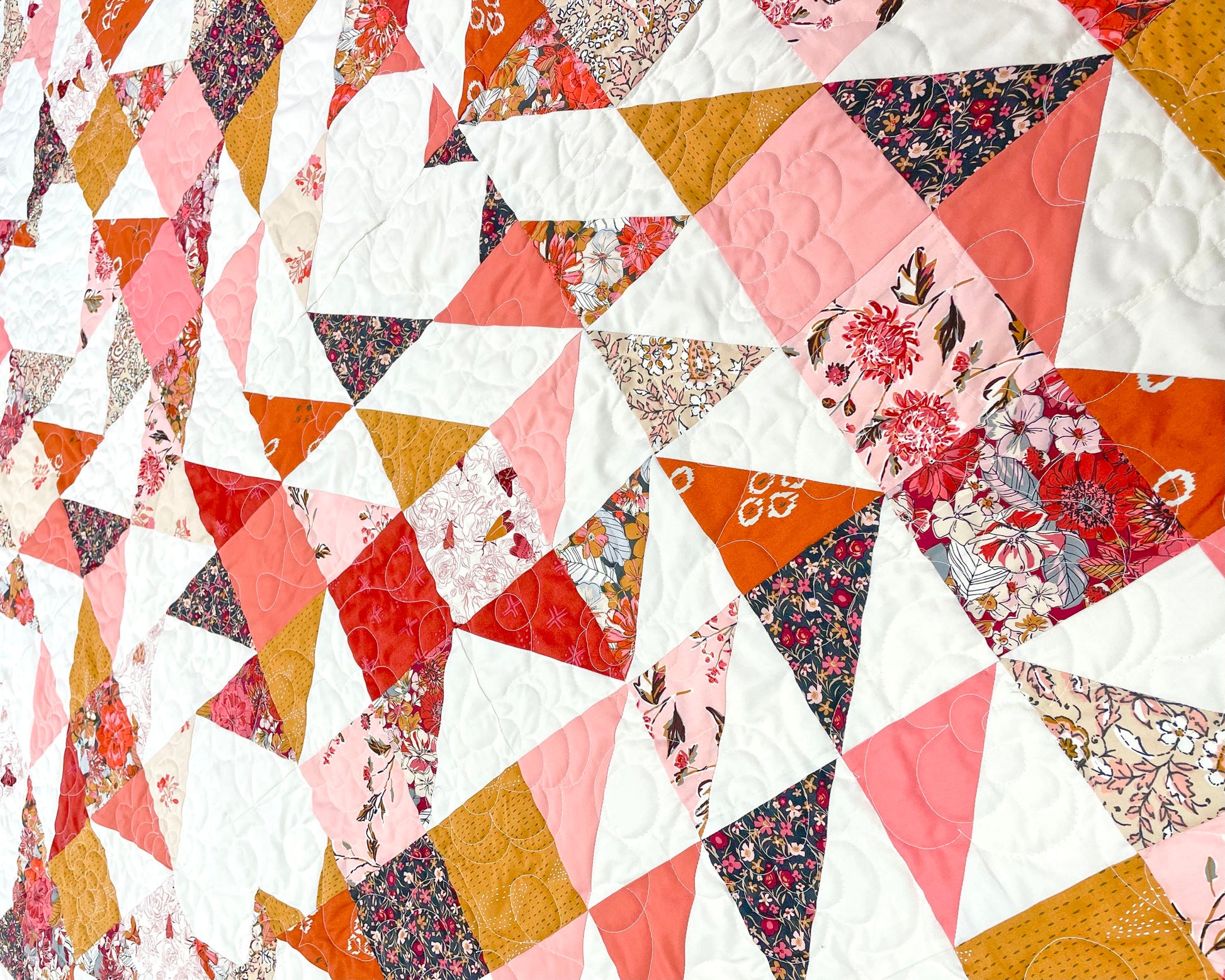 Sweet LaNora quilt. A geometric quilt with triangle and heart motifs made of fabric with red and peach tones.  A close up of a section of the quilt.