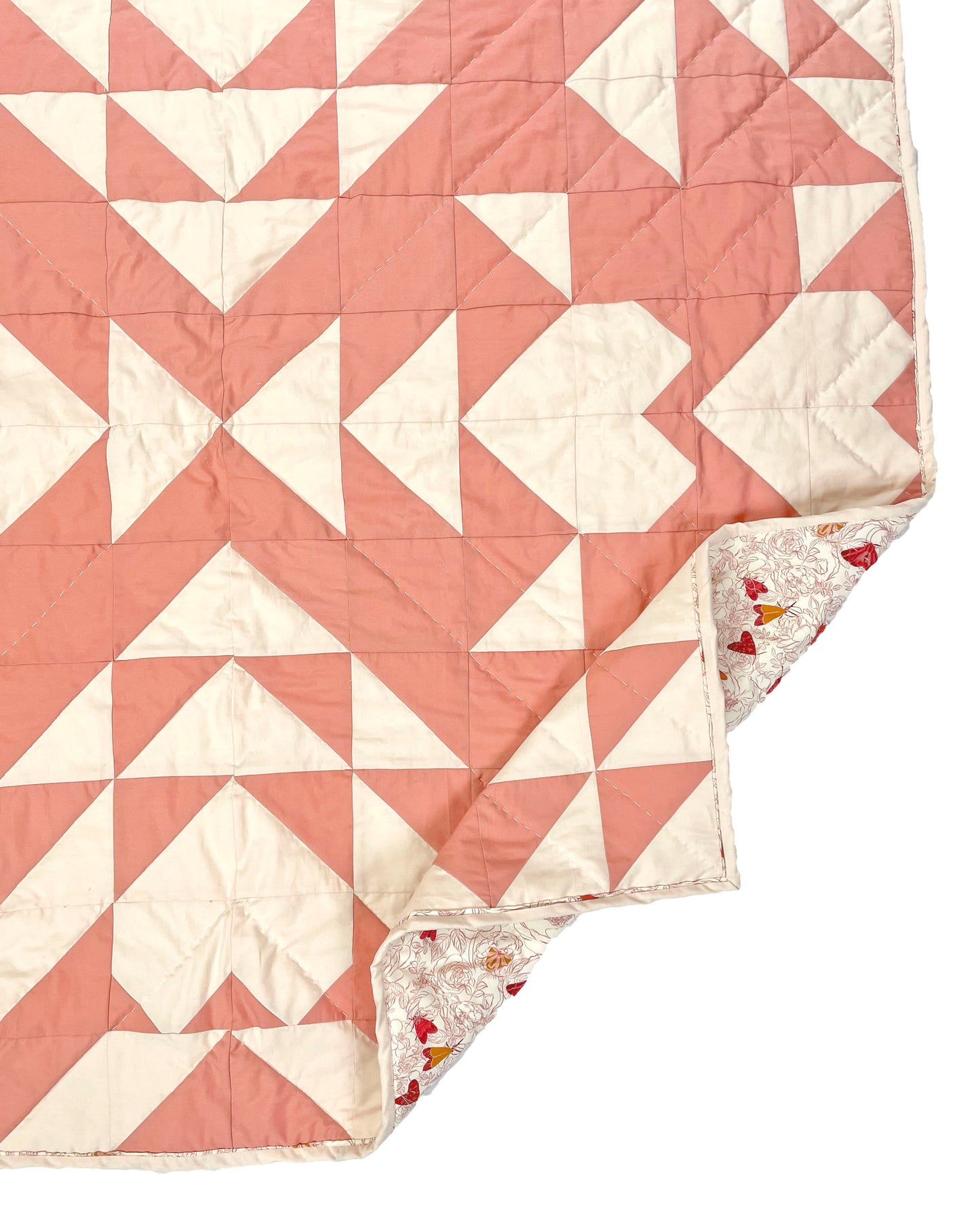 Sweet LaNora quilt. A geometric quilt with triangle and heart motifs made of fabric with ivory and peach tones.  Displayed flat on a white surface with the corner folded to show the backing fabric.