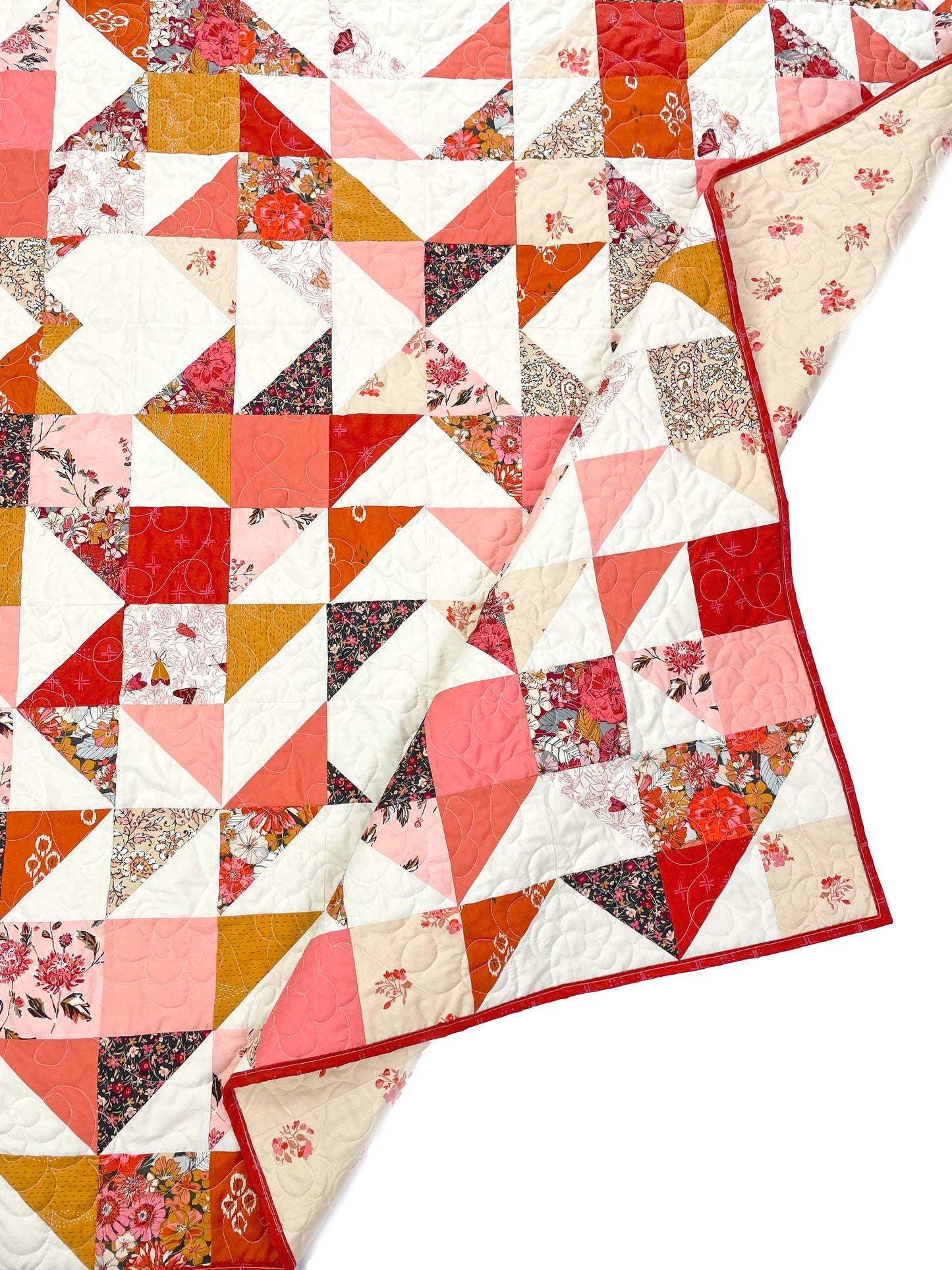 Sweet LaNora quilt. A geometric quilt with triangle and heart motifs made of fabric with red and peach tones.  Displayed flat on a white surface with the corner folded.