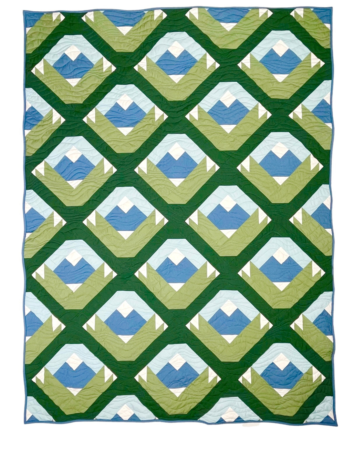 Wasatch quilt. A quilt with a repeating motif that appears similar to a mountain capped with snow above green strips. Blocks set on point. Made with green, blue, and white fabric. Displayed flat on a white surface.