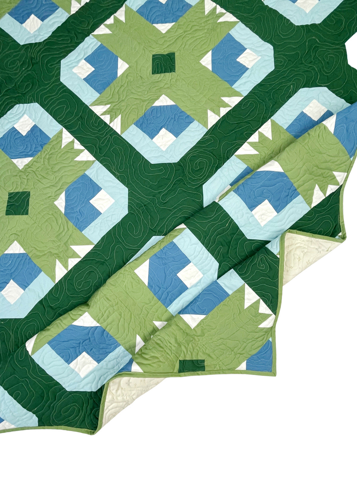 Wasatch quilt. A quilt with a repeating motif that appears similar to a mountain capped with snow above green strips. Blocks set on point. Rotated so blocks appear as a trellis design. Made with green, blue, and white fabric. Displayed flat on a white surface with the corner folded.